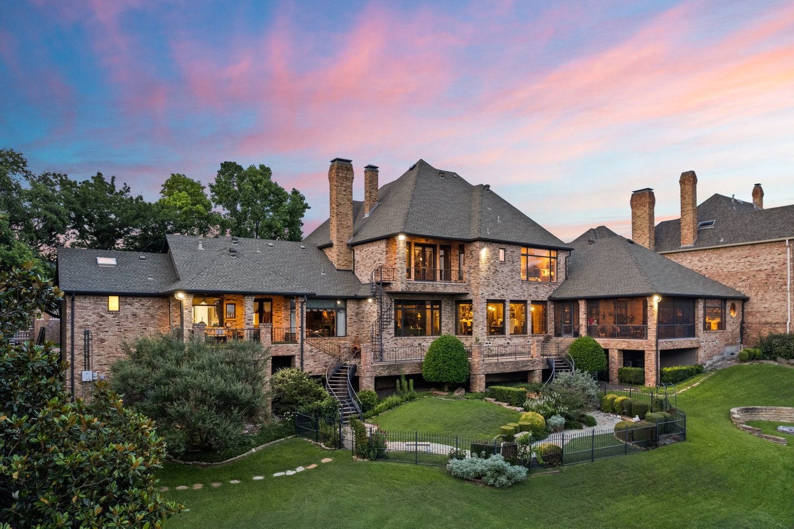 Brick estate with illuminated windows and landscaped gardens beneath a soft evening sky