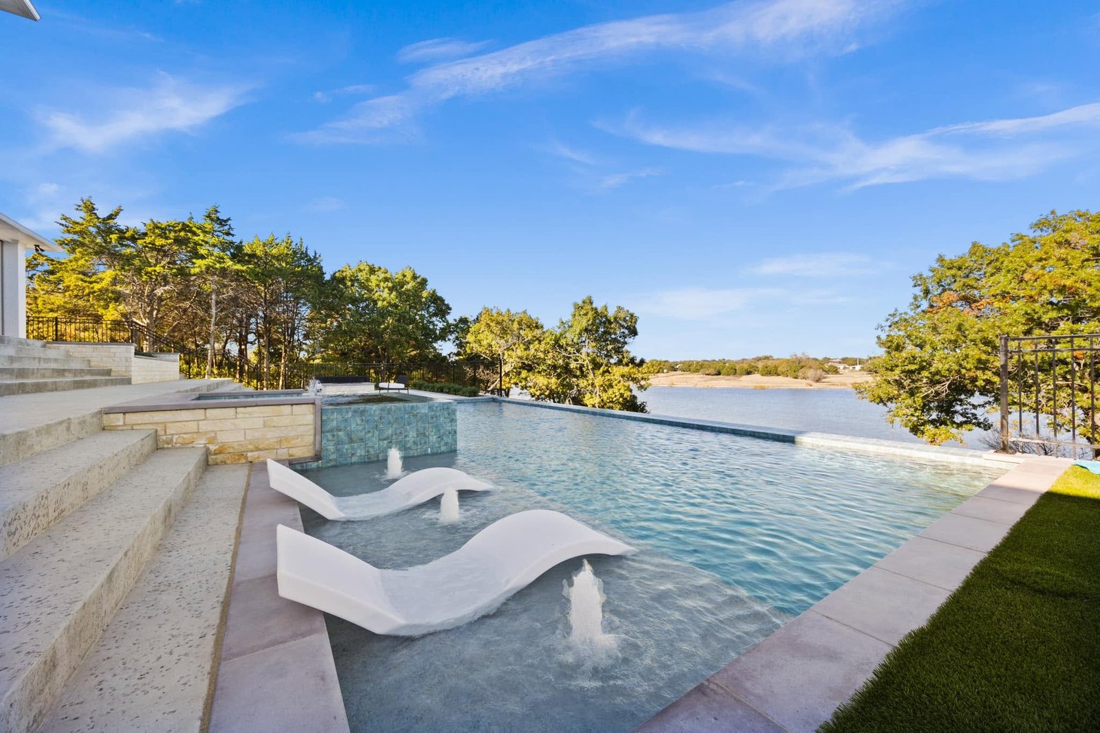 Infinity pool with white loungers and an expansive lake view