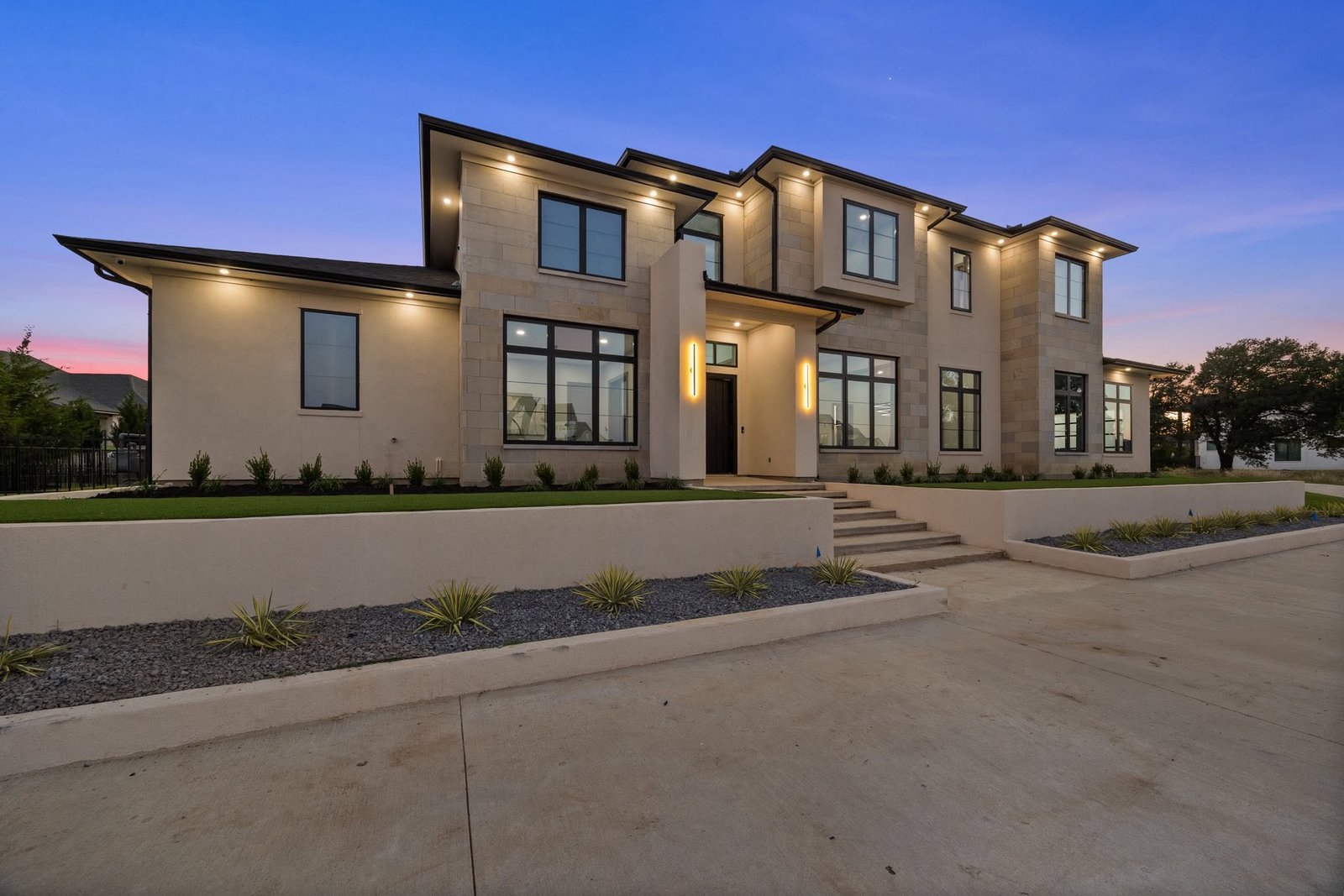 Modern stone and stucco home with warm architectural lighting at twilight